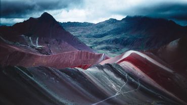 Colorful, layered mountain landscape under a moody cloudy sky.