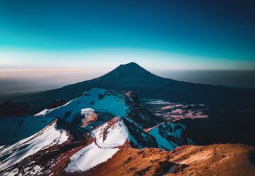 A majestic snow-capped mountain peak under a clear blue sky at dawn.