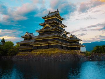 Historic Japanese castle reflecting in calm water at sunset.