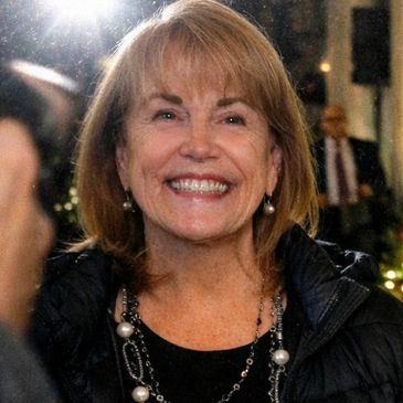 Smiling woman with pearl jewelry and a black jacket.