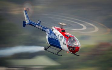 Blue, white, and red helicopter flying with a pilot visible.
