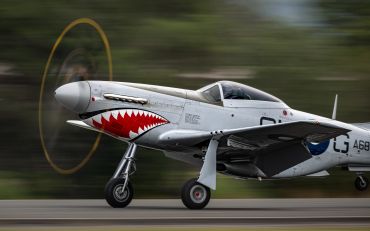 WWII-era fighter plane with shark mouth nose art taking off.