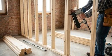 Carpenter using nail gun to frame a wooden wall inside a building.
