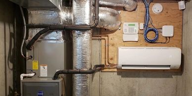 Modern HVAC system with ductwork and a wall-mounted control panel in a basement.