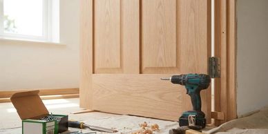Tools and screws on the floor beside a wooden door being installed.