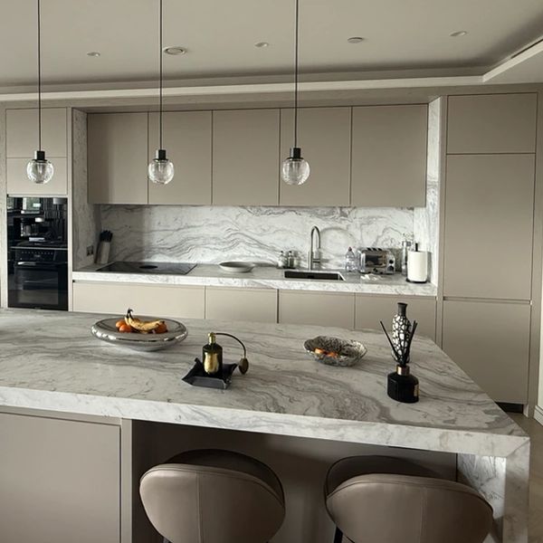 Modern kitchen with marble countertops and beige cabinets.