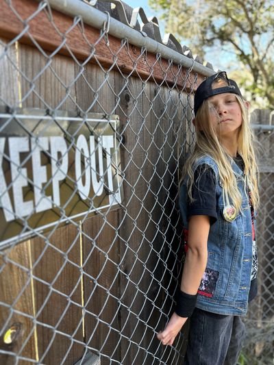 Young girl in casual punk style standing by a 'Keep Out' fence.