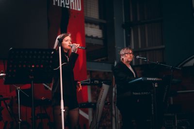 Two musicians performing on stage, one singing and one playing keyboard.