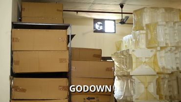 Stacked cardboard boxes and plastic containers in a storage room labeled 'GODOWN'.
