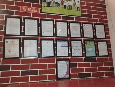 Wall display of various framed certificates in a waiting area with faux brick background.