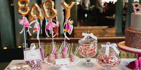 A festive baby shower dessert table with pink decorations and treats.