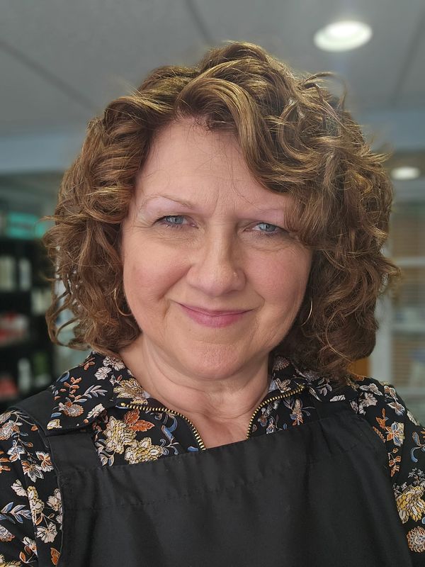 Smiling middle-aged woman with curly hair in a floral shirt and black apron.