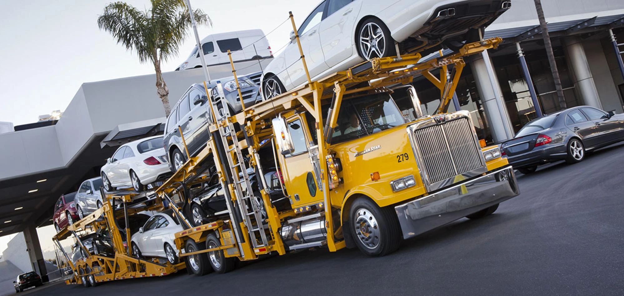 Yellow car carrier truck loaded with multiple cars on a city street.