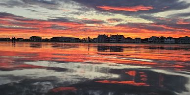 Sunset over calm water with silhouetted buildings.