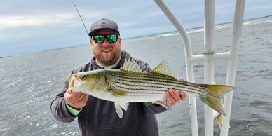 Man holding a striped bass on a boat.