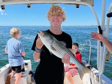 Teen boy holding a striped bass on a fishing boat.