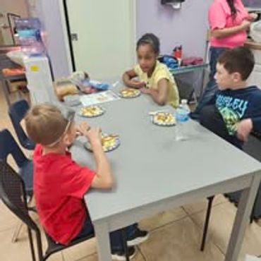Three children sitting at a table eating snacks.