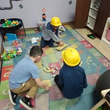 Three kids wearing yellow construction hats playing with blocks indoors.