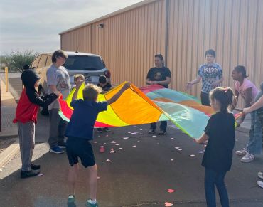 Children playing with a colorful parachute outdoors on a sunny day.