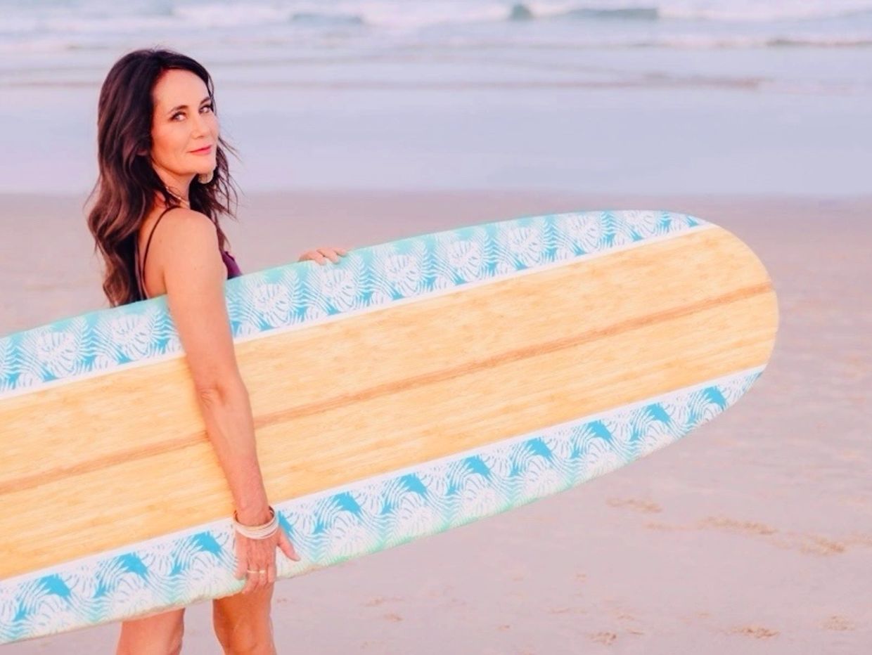 Woman holding a decorative surfboard at the beach.