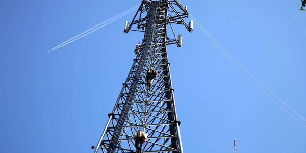 Two workers climbing a tall communication tower against a clear sky.