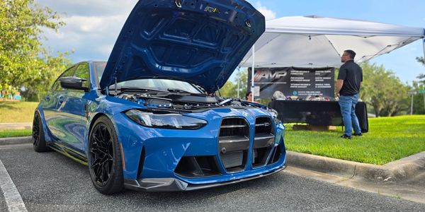 Blue BMW M4 with hood open at an outdoor car event.