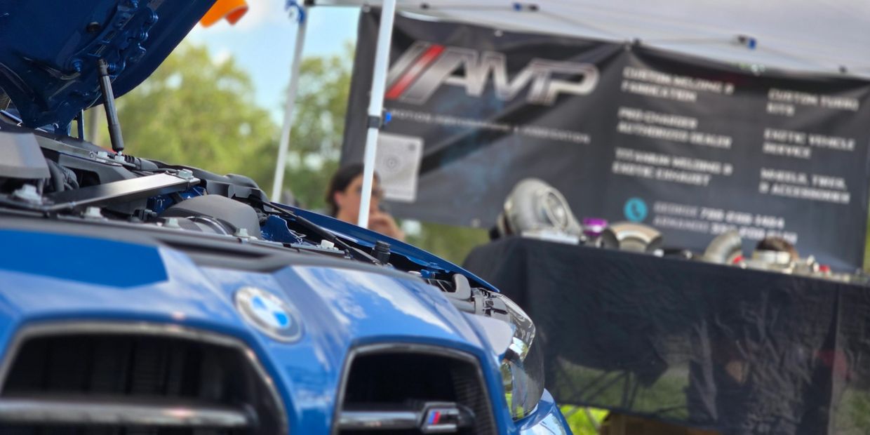 Close-up of a blue BMW with hood open at a car event booth.