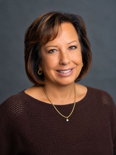 Smiling woman with short brown hair and gold jewelry.