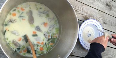 A big casserole with fish soup and hands cleaning a piece of fish