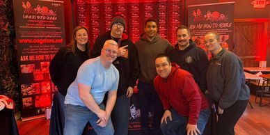 A group of seven people posing indoors with red promotional banners in the background.