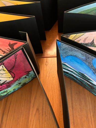 A colorful accordion-fold artist's book open on a wooden table seen from above.