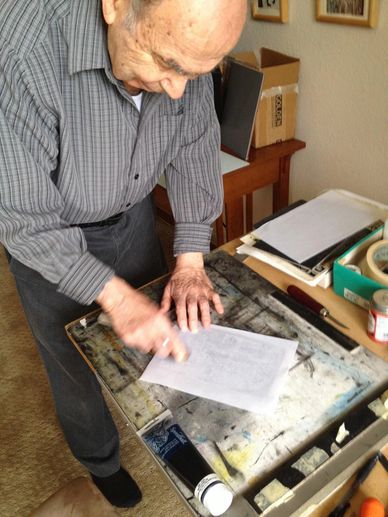 An older male artist hand-burnishing a linoleum block print.