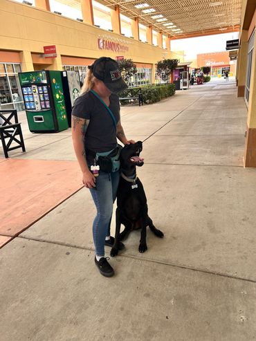 Woman petting a happy black dog outside a shopping mall.