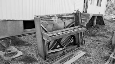 An old, broken piano standing outside near a building.