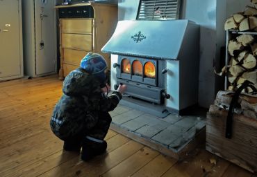 Child warming hands near a wood stove in a cozy room.