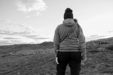 Person standing on a hill, looking at a distant flock of sheep in a black and white photo.