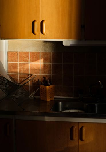 Sunlight casts warm shadows in a kitchen with wooden cabinets and tiled backsplash.
