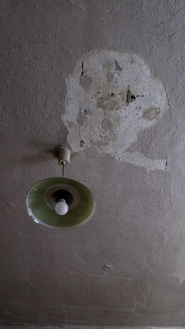 Old ceiling lamp with peeling plaster around it.