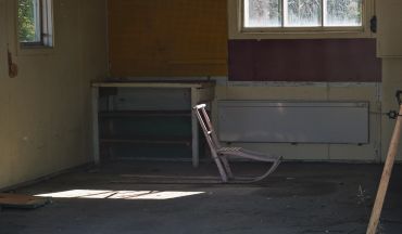 An empty room with a wooden rocking chair and sunlight streaming through a window.