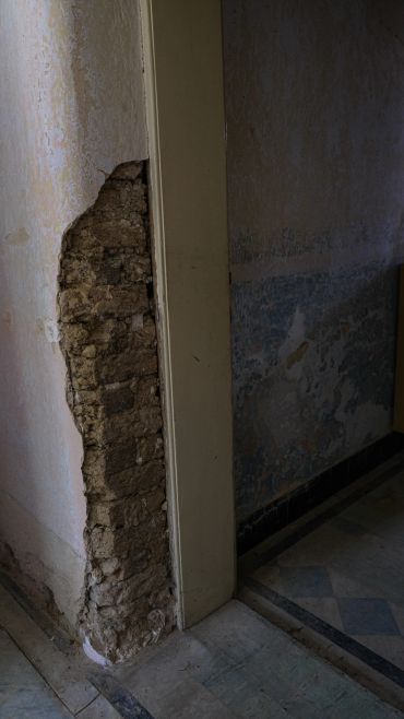 A wall with plaster crumbling to reveal underlying bricks in a dimly lit room.