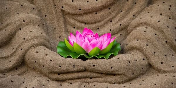 Statue in Meditationspose sitzend mit blühendem Lotus in der Hand.