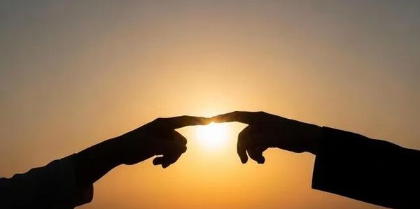 Zwei Hände, die sich im Sonnenuntergang berühren und so menschliche Verbindung symbolisieren 