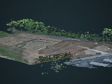 Aerial view of a terrain with vegetation and a paved area near water.