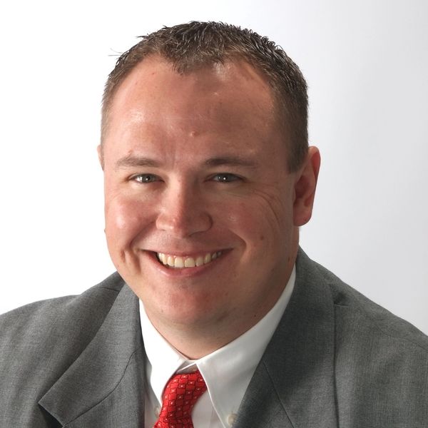 Smiling man in a gray suit and red tie against a white background.