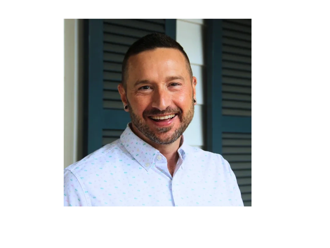 Smiling man with short hair and beard in white shirt.