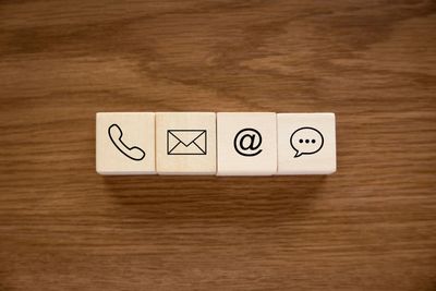 Four cubes with icons for phone, postal address, email and, on a wooden surface