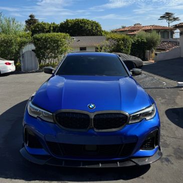 Blue BMW parked on a driveway under clear sky.