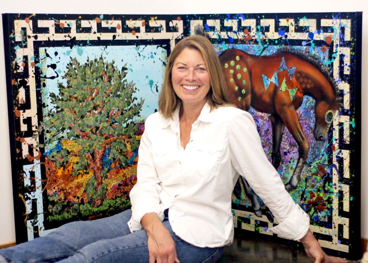The artist Liz Chappie-Zoller seated in front of two of her mixed media paintings