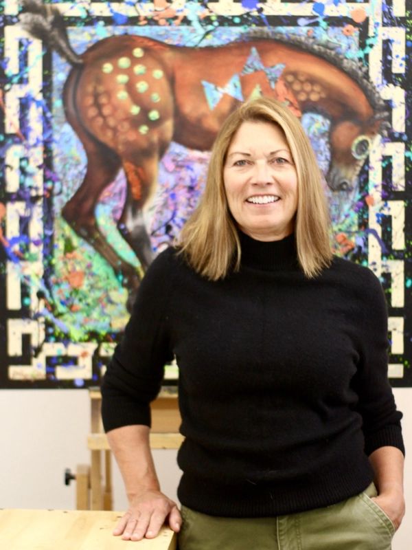 The artist Liz Chappie-Zoller standing in her studio in front of a horse painting