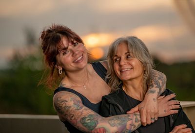 Two women embracing and smiling warmly outdoors at sunset.